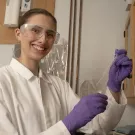 Brook wears a lab coat, gloves and safety glasses while holding a test tube