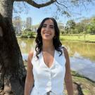Nana Moraes, PhD candidate in Anthropology, smiling in a white outfit at a park